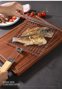 Foldable stainless steel grill basket with wooden handle showing grilled fish in a kitchen