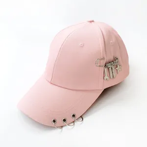 Pink baseball cap with metal rings and safety pin charms featuring a razor blade design.