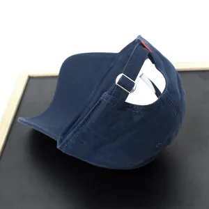 Detail view of navy blue baseball cap back strap with metal adjustable buckle and red tab.