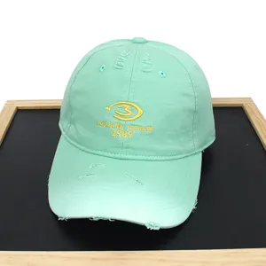 Close-up detail of mint green distressed baseball cap featuring yellow letter embroidery