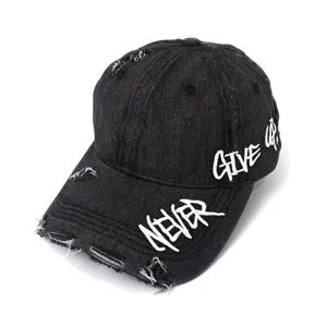 Dettaglio del cappello da baseball in denim lavato nero con ricamo e dettagli strappati.