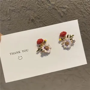 Close-up of delicate pastoral floral stud earrings with rhinestones on a card.