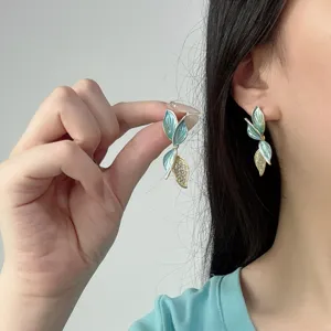 Primo piano di orecchini a foglia in smalto blu con dettagli in strass lucidi.