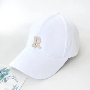 Close-up of a stylish white baseball cap featuring a beige 'R' letter embroidery detail
