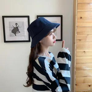 Detailed view of a navy blue bucket hat worn by a model in a stylish indoor setting.