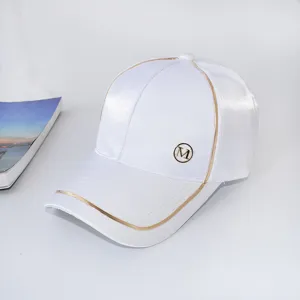 White baseball cap with stylish gold piping and metal M logo detail, perfect for summer sun.