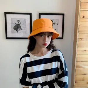 Close-up of an Asian model wearing a bright orange minimalist cotton bucket hat indoors