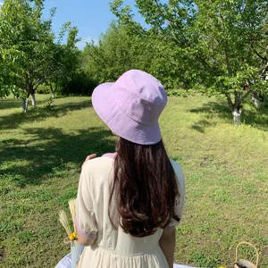 A simple minimalist light purple bucket hat for women shown in a sunny outdoor garden setting