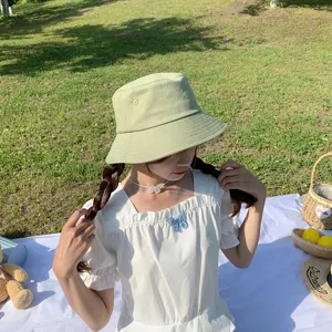 Young woman wearing a sage green minimalist bucket hat during a sunny outdoor picnic scene