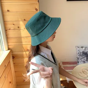 Detailed side view of a dark green cotton bucket hat worn by a model in soft sunlight.