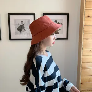 Side profile detail of an Asian woman wearing a terracotta cotton bucket hat indoors