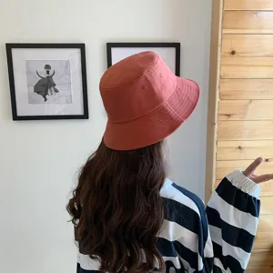 Back view of a girl wearing a stylish burnt orange bucket hat in a cozy indoor room