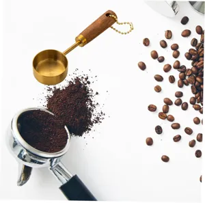 Gold-plated stainless steel coffee measuring spoon with wooden handle near coffee beans