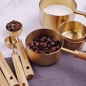 Détail de tasses à mesurer en inox or rose avec manches en bois et gravures