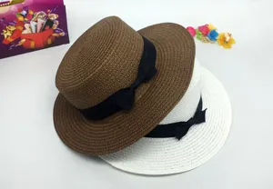 Detail view of a stylish women's flat top straw hat with a classic black bow ribbon.
