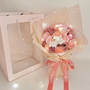 Detailed view of handmade soap rose and carnation bouquet with warm LED string lights and gift bag.