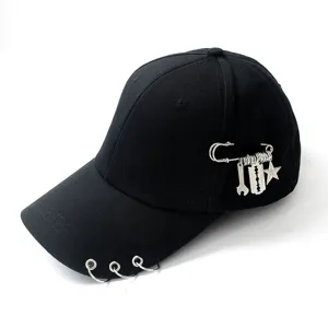 Close-up of a black baseball cap with silver rings on brim and safety pin charms.