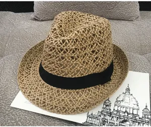 Close-up of a woven straw fedora sun hat with a black ribbon band on a textured background