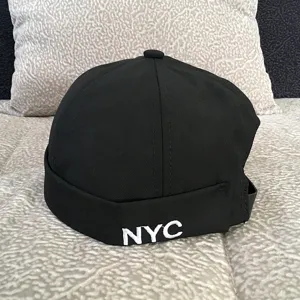 Black dome dockman cap detail, minimalist brimless hat with white NYC embroidery, streetwear.