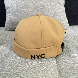Detail view of a khaki brimless docker cap with black NYC embroidery and adjustable back strap.