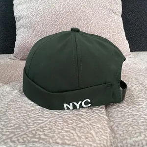 Green denim docker cap detail shot, stylish brimless miki hat with white NYC embroidery.