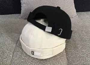 Detail view of black and white dockier hats stacked together, showing brand label and strap.