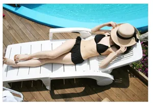 Woman wearing a large brim straw hat while relaxing on a sun lounger by the pool