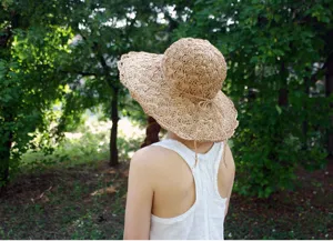 Rear view of a woman wearing a wide brim straw sun hat in a lush green garden setting