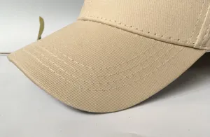Close-up of the reinforced stitching on the brim of a beige cotton baseball cap.