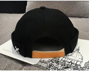 Black dockworker cap with metal cross detail, trendy street style brimless melon hat for daily wear.