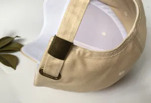 Detailed view of the adjustable metal buckle and stitching on a beige cotton baseball cap