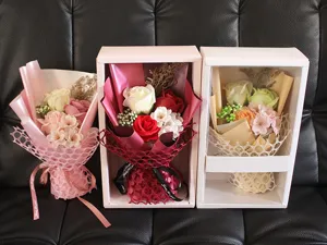 Detail von drei bunten Seifenblumensträußen in eleganten Geschenkboxen auf schwarzem Grund