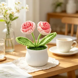 Close-up of handmade pink crocheted roses in a white ceramic pot on a sunlit desk.