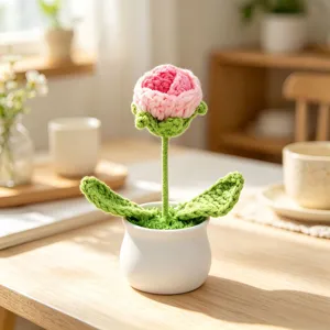 Close-up of a handmade pink crocheted flower in a white pot on a wooden desk surface