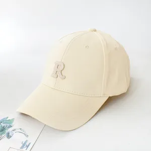 Close-up detail of a cream-colored baseball cap with an embroidered letter R logo