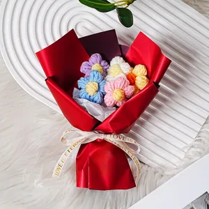 Ramo de flores de ganchillo hechas a mano como regalo, papel de envolver rojo y cinta decorativa.