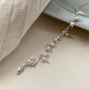 Detalle de una pulsera minimalista de plata con perlas lavanda sobre tela beige suave