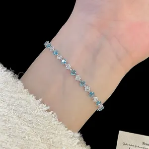 Macro detail of a delicate silver bracelet with blue and clear square zirconia on a wrist.