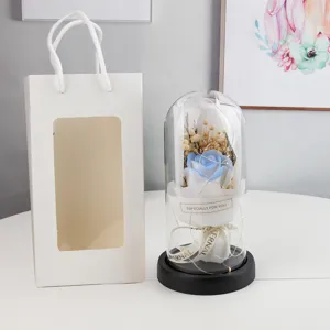 Exquisite preserved blue rose in glass dome detail view with romantic fairy lights and gift bag.