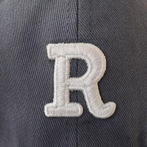 Close-up detail of high-quality white embroidered letter R on a grey cotton baseball cap