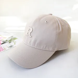 Detailed macro view of a stylish beige baseball cap featuring a white embroidered R letter logo.
