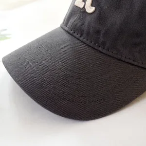 Close-up detail of a dark grey cotton baseball cap featuring a white embroidered R letter
