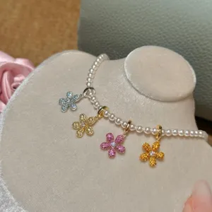 Close-up of colorful zircon daisy pendants on a white pearl necklace, DIY jewelry design.