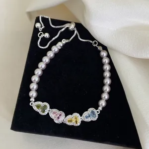 Primer plano de elegante pulsera de perlas con dijes de circonita de colores en forma corazón