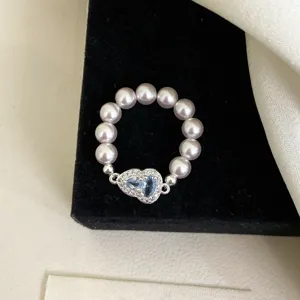 Primer plano de un elegante anillo elástico de perlas con un colgante de corazón de circón azul.