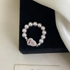 Primer plano de un anillo elástico de perlas rosas con un dije brillante en forma de calabaza.