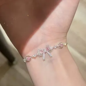 Dettaglio di un bracciale con fiocco rosa e pietre di zirconia a forma di cuore al polso