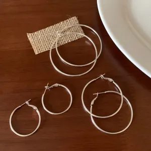Dettaglio di tre paia di orecchini a cerchio sottili in argento di varie misure.