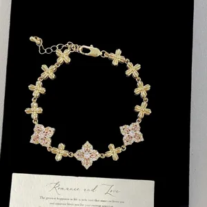 Close-up of gold bracelet featuring pink and clear crystal four-leaf flower charms.