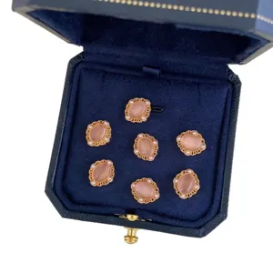 Vintage ornate gold-tone oval buttons with peach gems in a navy blue jewelry box